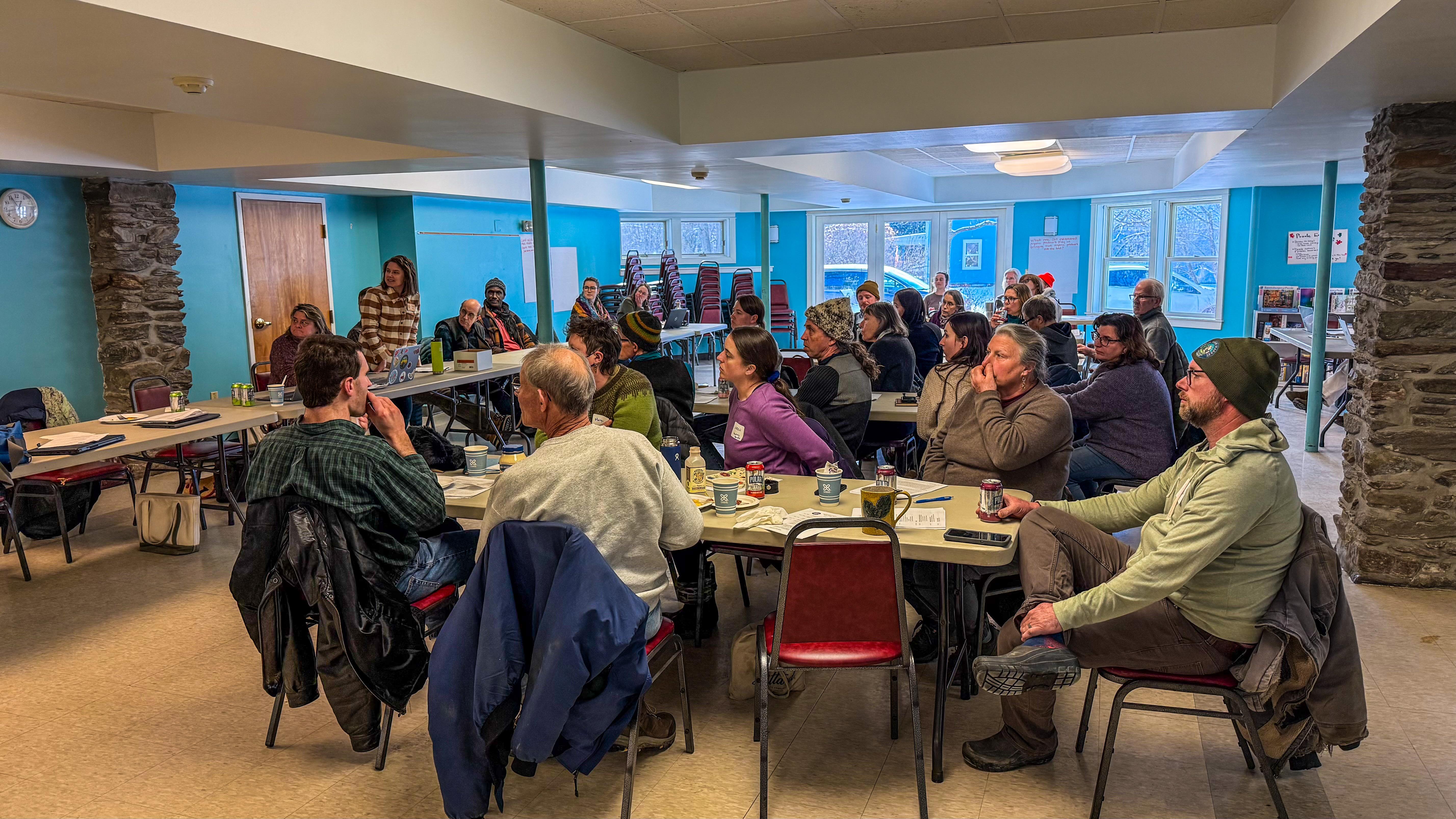 A group of farmers gathered around tables listening to a presentation at the 2026 Vermont Organic Farmers (VOF) Annual Producers' Meeting